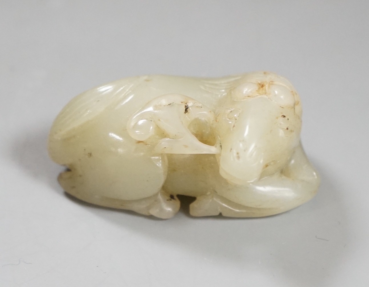 A 19th century Chinese pale celadon jade figure of a seated horse, 6cm wide